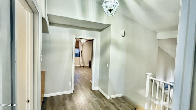 corridor with an upstairs landing, baseboards, and wood finished floors