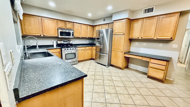 kitchen with dark countertops, visible vents, built in desk, appliances with stainless steel finishes, and a sink