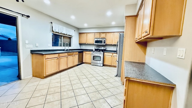 kitchen with light brown cabinets, recessed lighting, a sink, stainless steel appliances, and dark countertops