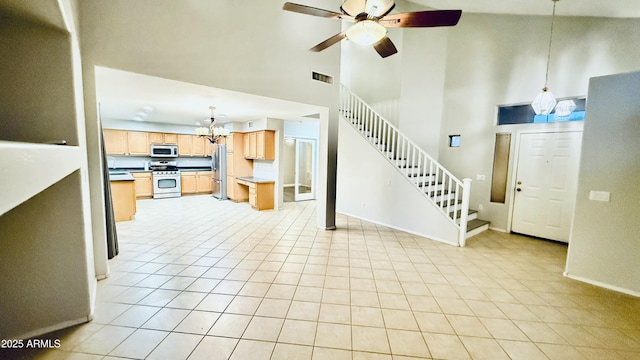 unfurnished living room featuring baseboards, visible vents, stairs, a towering ceiling, and ceiling fan with notable chandelier