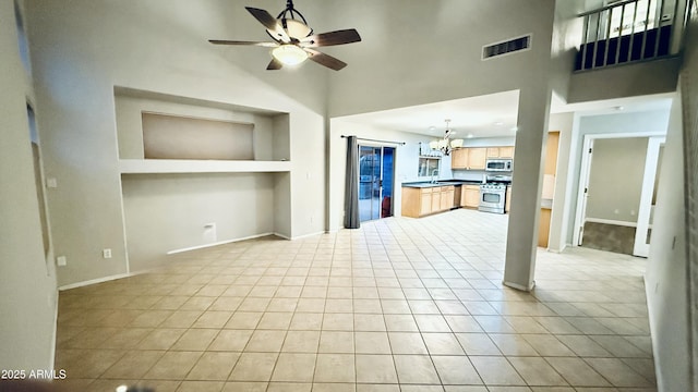 unfurnished living room featuring visible vents, built in shelves, ceiling fan with notable chandelier, a towering ceiling, and light tile patterned flooring