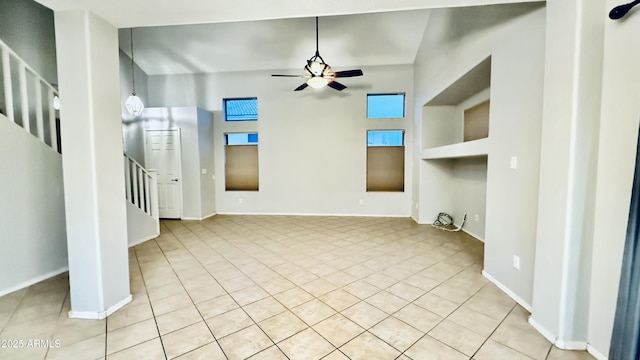 unfurnished living room featuring light tile patterned flooring, baseboards, ceiling fan, and stairs