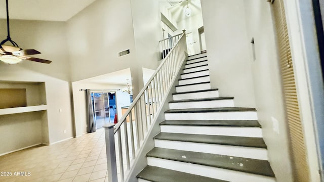 staircase with visible vents, ceiling fan with notable chandelier, a high ceiling, tile patterned flooring, and baseboards