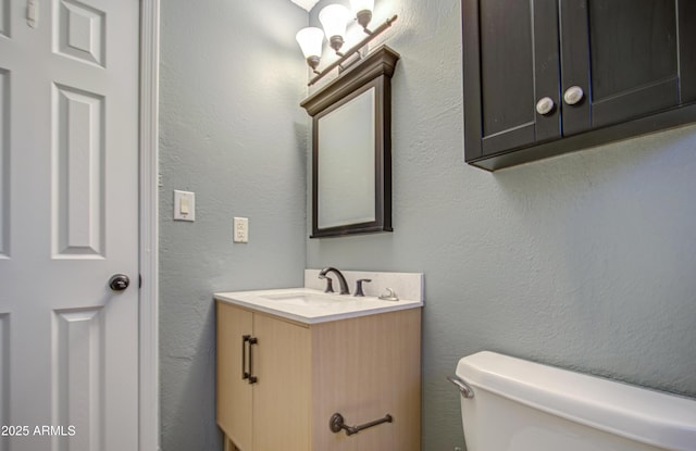 bathroom with toilet, vanity, and a textured wall