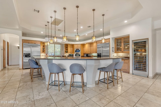 kitchen with a raised ceiling, stainless steel built in refrigerator, and hanging light fixtures