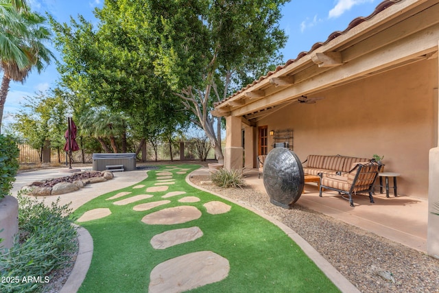 view of yard featuring ceiling fan, an outdoor living space, a hot tub, and a patio area