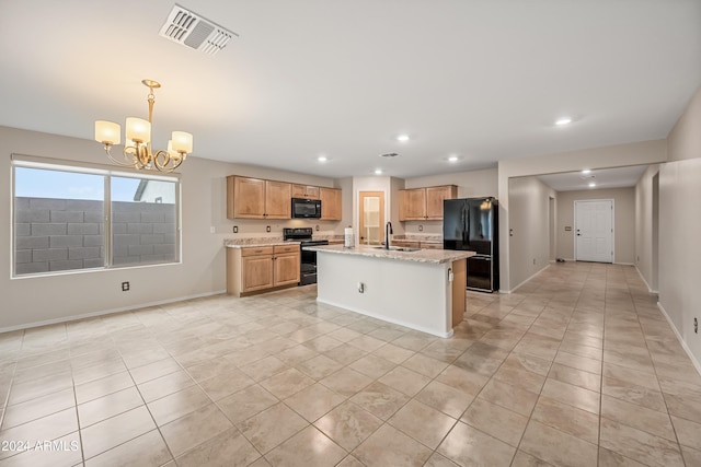 kitchen featuring black appliances, sink, light stone countertops, an island with sink, and a notable chandelier