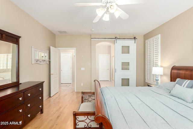 bedroom with light wood finished floors, a barn door, visible vents, and a ceiling fan