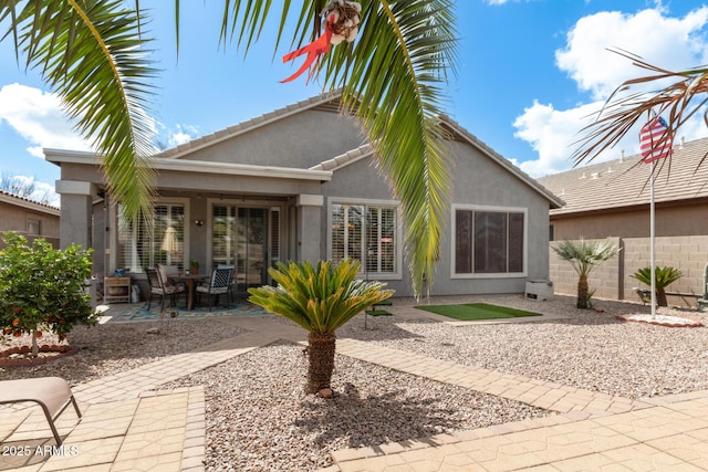 rear view of property featuring a tiled roof, a patio, fence, and stucco siding