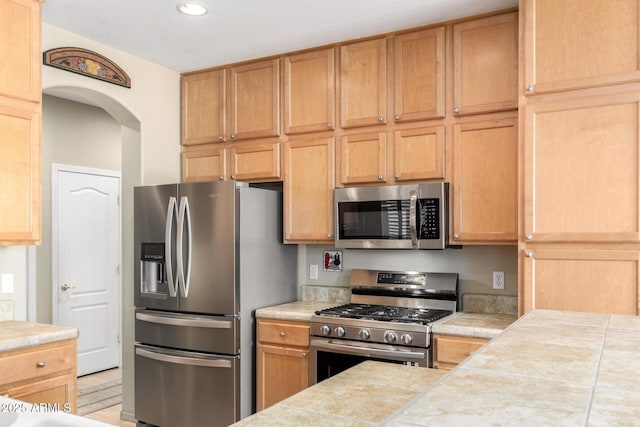 kitchen featuring arched walkways, tile countertops, and appliances with stainless steel finishes