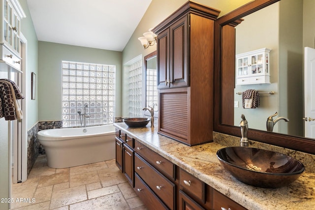 bathroom featuring stone tile floors, a soaking tub, lofted ceiling, and a sink