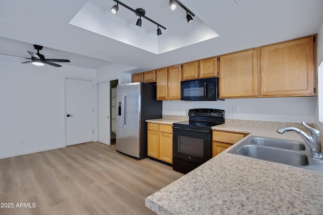 kitchen featuring black appliances, light countertops, a tray ceiling, and a sink