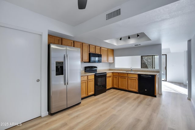 kitchen featuring black appliances, a sink, a tray ceiling, light wood-style floors, and light countertops