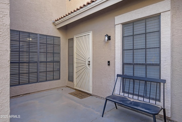 property entrance with a patio area, stucco siding, and a tiled roof