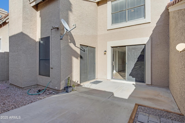 view of exterior entry with a patio area, fence, and stucco siding