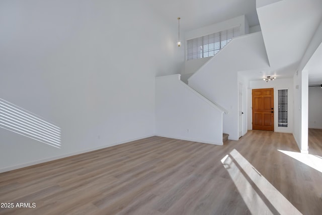 unfurnished living room with stairway, baseboards, light wood-type flooring, and a high ceiling