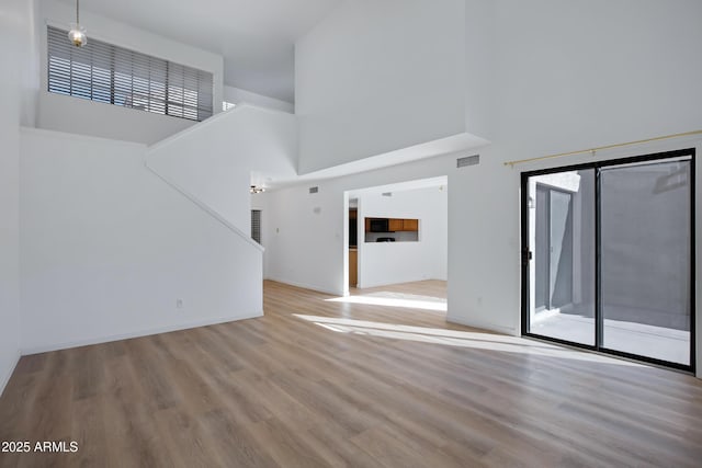 unfurnished living room featuring a high ceiling, wood finished floors, and visible vents