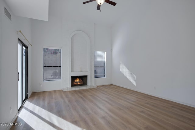 unfurnished living room with visible vents, ceiling fan, a fireplace, a high ceiling, and wood finished floors