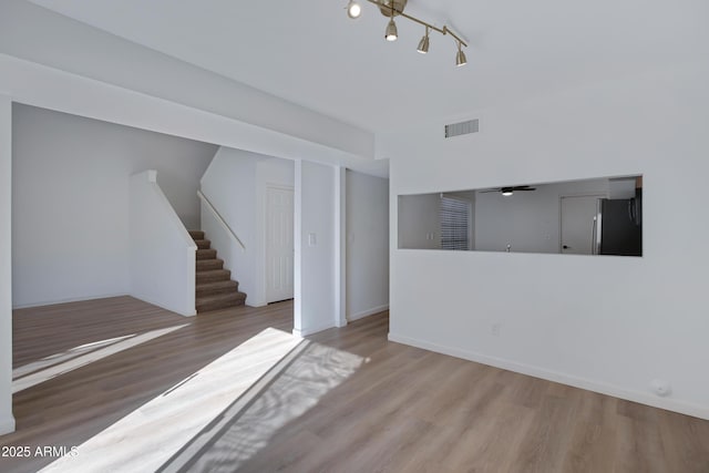 unfurnished living room featuring visible vents, baseboards, wood finished floors, and stairs