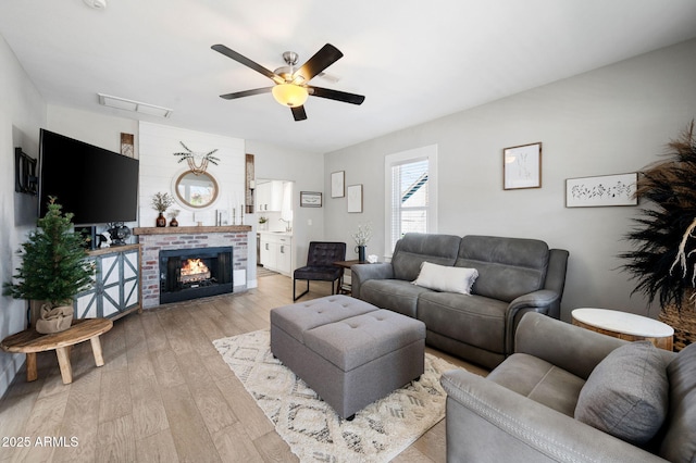 living area with a fireplace, a ceiling fan, visible vents, and light wood finished floors