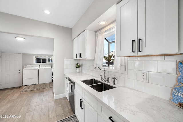 kitchen featuring washing machine and clothes dryer, a sink, backsplash, light stone counters, and stainless steel dishwasher