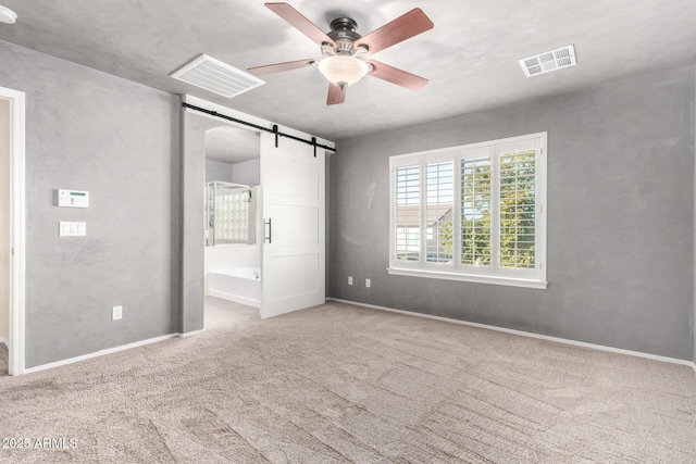 unfurnished bedroom featuring ensuite bathroom, a barn door, carpet floors, and ceiling fan