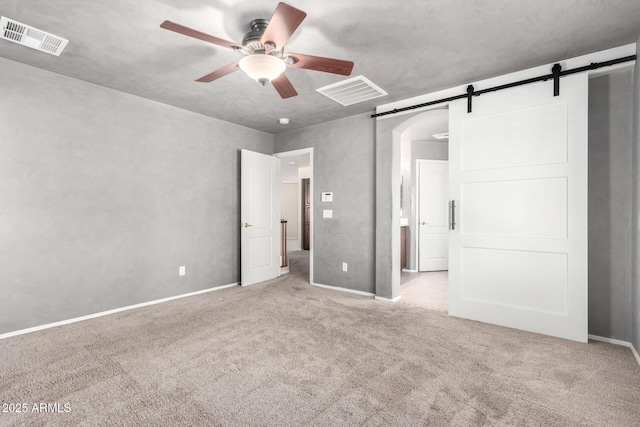 unfurnished bedroom featuring ceiling fan, a barn door, and light colored carpet