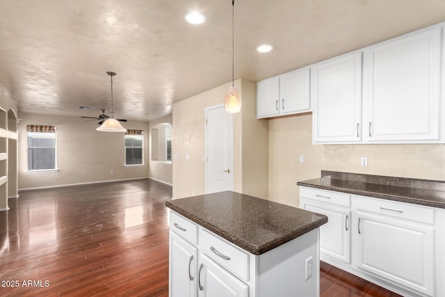 kitchen with dark wood-type flooring, ceiling fan, hanging light fixtures, a center island, and white cabinets