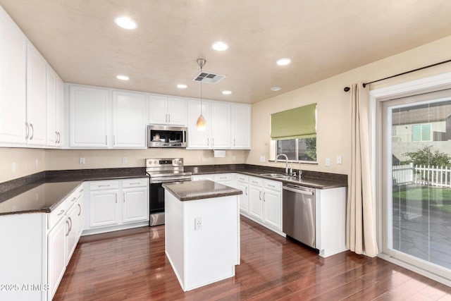 kitchen with sink, stainless steel appliances, white cabinets, a kitchen island, and decorative light fixtures