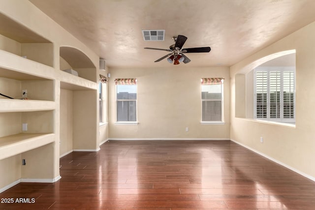 empty room featuring ceiling fan, built in features, dark hardwood / wood-style floors, and a healthy amount of sunlight