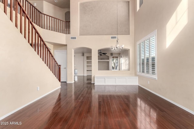 unfurnished living room with a towering ceiling, ceiling fan with notable chandelier, and dark hardwood / wood-style flooring