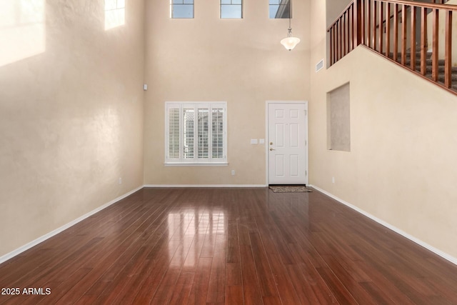 unfurnished living room featuring a towering ceiling and dark hardwood / wood-style flooring