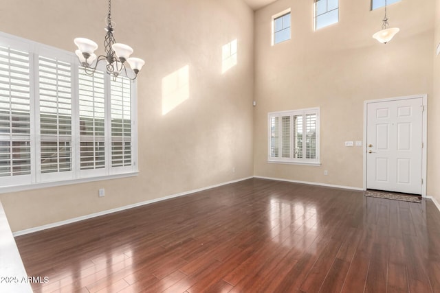 unfurnished living room featuring a notable chandelier, a towering ceiling, and dark hardwood / wood-style floors