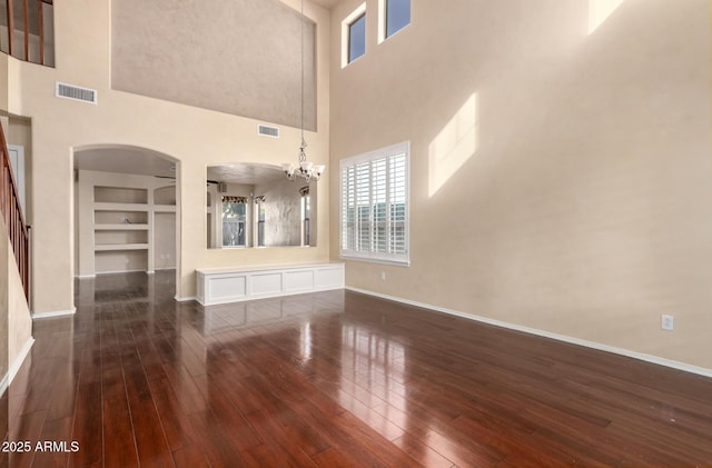 unfurnished living room featuring a high ceiling, a chandelier, dark hardwood / wood-style flooring, and built in shelves