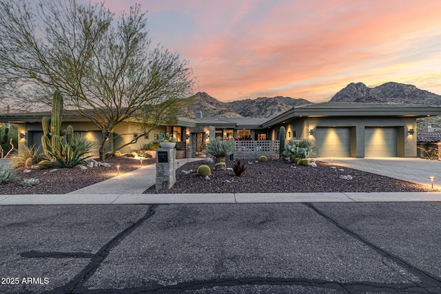 prairie-style house with stucco siding, an attached garage, driveway, covered porch, and a mountain view