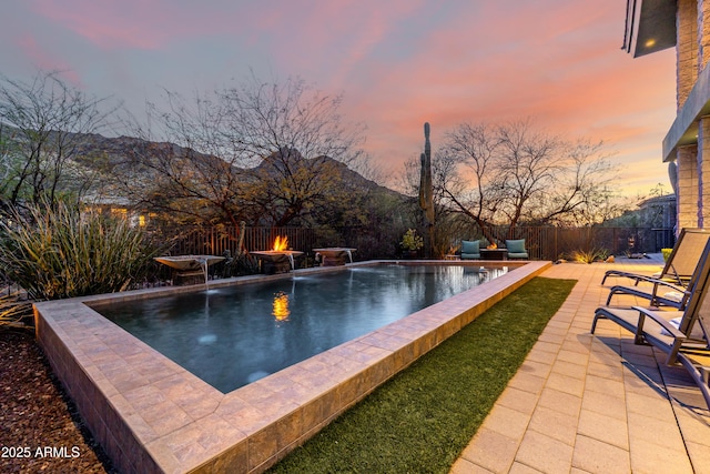 pool at dusk featuring a fenced in pool, a patio area, a fenced backyard, and a mountain view