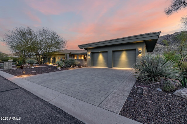 prairie-style home featuring stucco siding, an attached garage, and decorative driveway