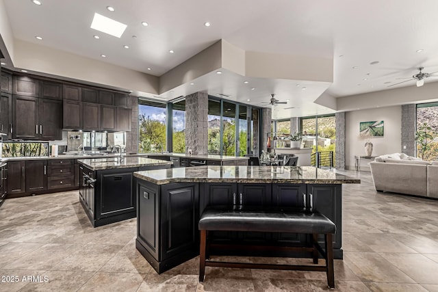 kitchen with open floor plan, recessed lighting, stone countertops, ceiling fan, and an island with sink