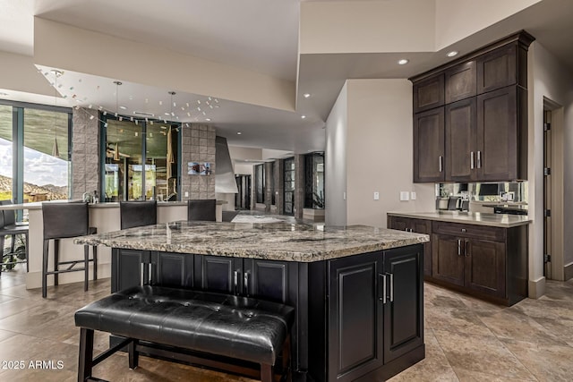 kitchen with dark brown cabinets, a spacious island, light stone countertops, and recessed lighting