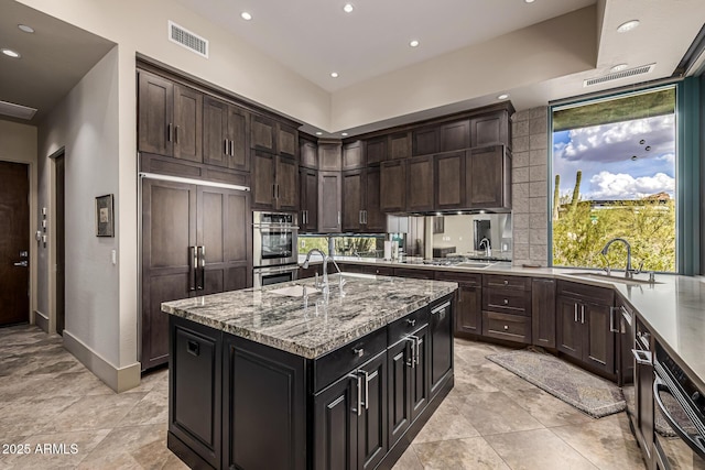 kitchen featuring recessed lighting, paneled fridge, light stone counters, visible vents, and a sink