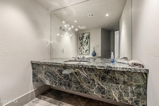 bathroom with vanity, a textured wall, stone finish floor, and visible vents