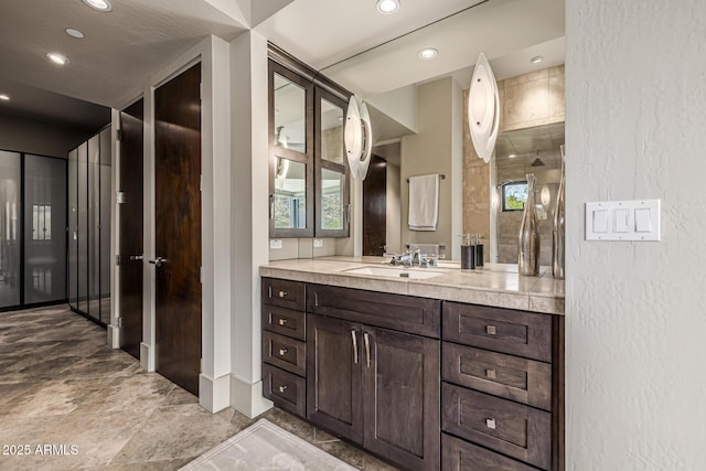 bathroom featuring recessed lighting, a textured wall, and vanity
