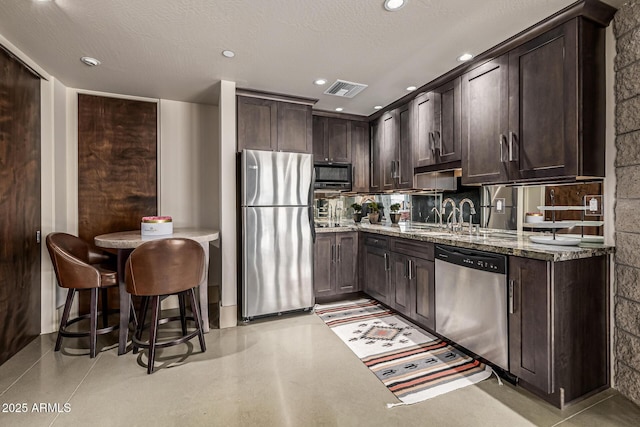 kitchen with light stone counters, dark brown cabinets, visible vents, a sink, and appliances with stainless steel finishes