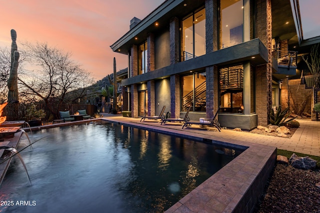 back of property at dusk with a fenced in pool, a patio, a balcony, and fence
