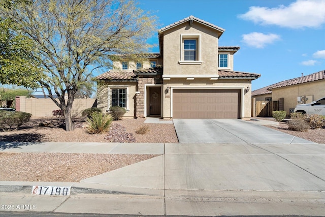 mediterranean / spanish home with concrete driveway, a tiled roof, an attached garage, fence, and stucco siding