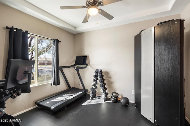 exercise room featuring a raised ceiling, a ceiling fan, and baseboards