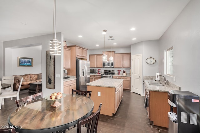 kitchen with sink, hanging light fixtures, appliances with stainless steel finishes, a kitchen island, and light stone countertops