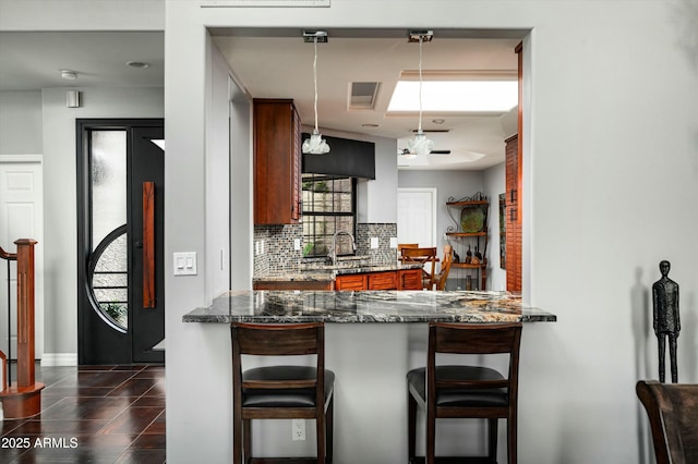 kitchen featuring a peninsula, a sink, hanging light fixtures, a kitchen breakfast bar, and tasteful backsplash