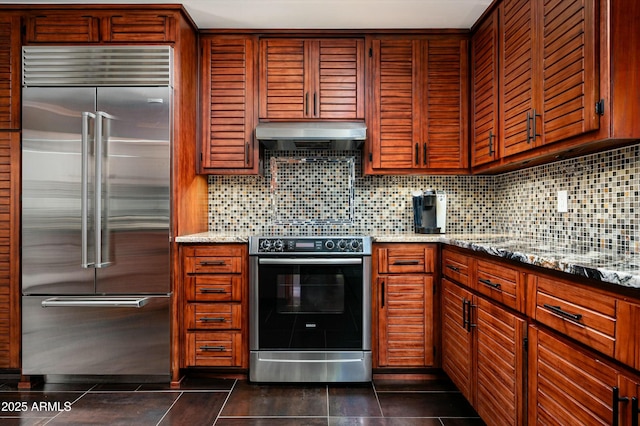 kitchen featuring under cabinet range hood, light stone counters, backsplash, and appliances with stainless steel finishes