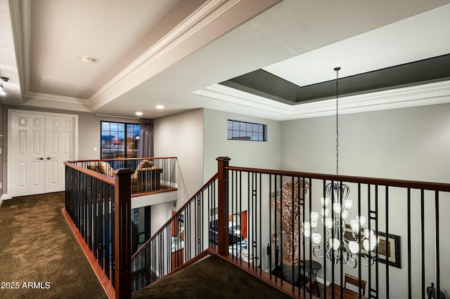 corridor with crown molding, carpet, an upstairs landing, an inviting chandelier, and a raised ceiling